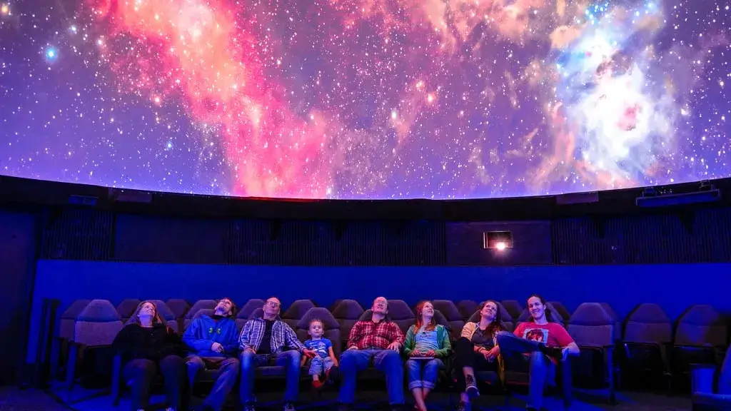 Interior view of a state-of-the-art planetarium dome showcasing a vivid projection of the night sky, surrounded by engaged visitors.